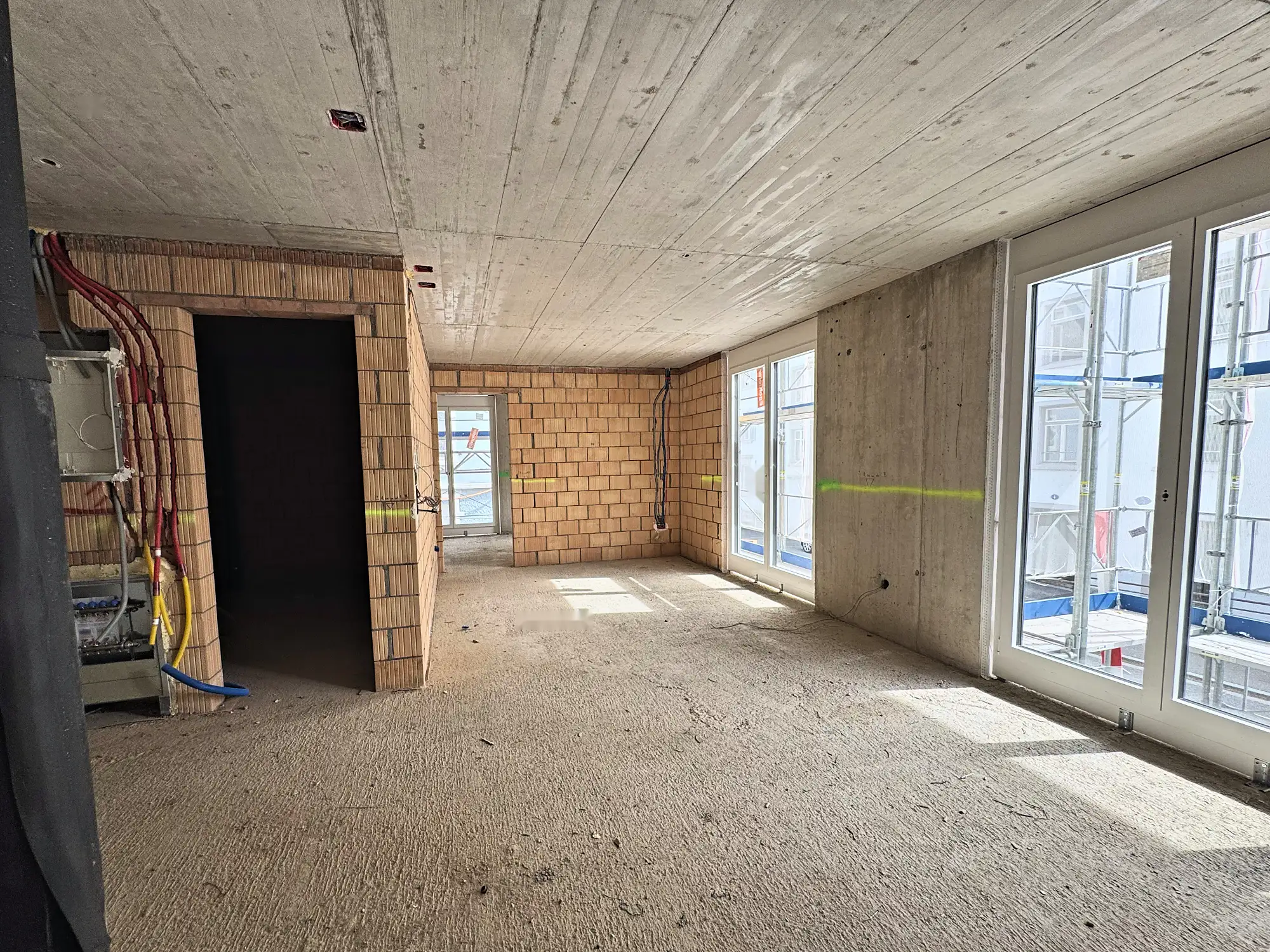 Wohnraum im Rohbau mit Backsteinwand, Sichtbetondecke und Fensterfront