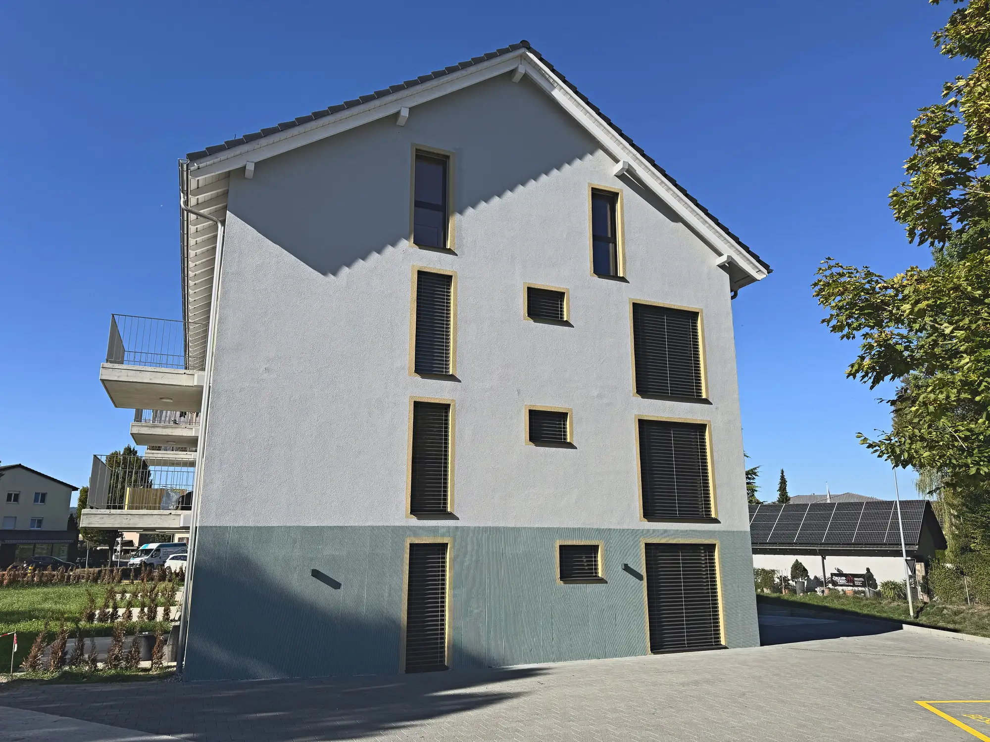 Giebelfassade mit versetzten Fensteröffnungen, davor der gepflasterte Vorplatz