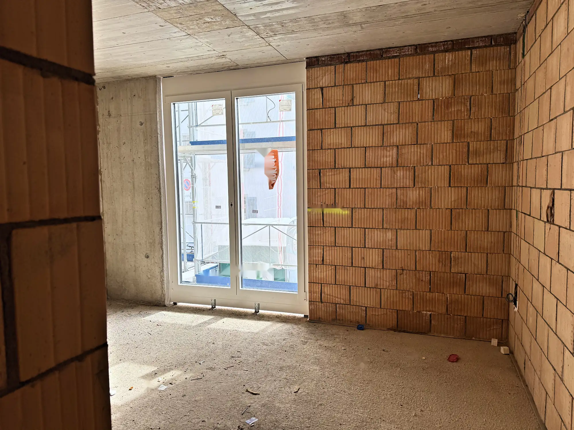 Raum im Rohbau mit Backsteinmauerwerk und bodentiefem Fenster