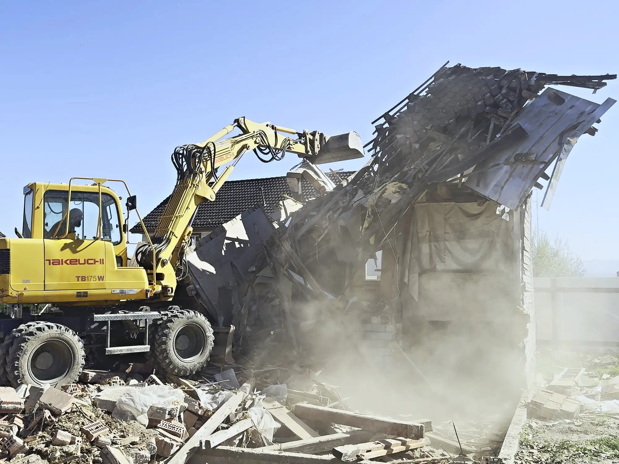 Bagger reisst die Fassade eines Altbaus ein, Staubwolke davor