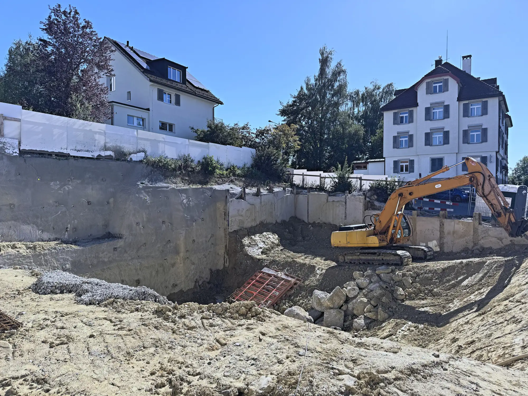 Bagger auf der Rampe zwischen Baugrube und Rühlwand, bewohnte Nachbarhäuser dahinter