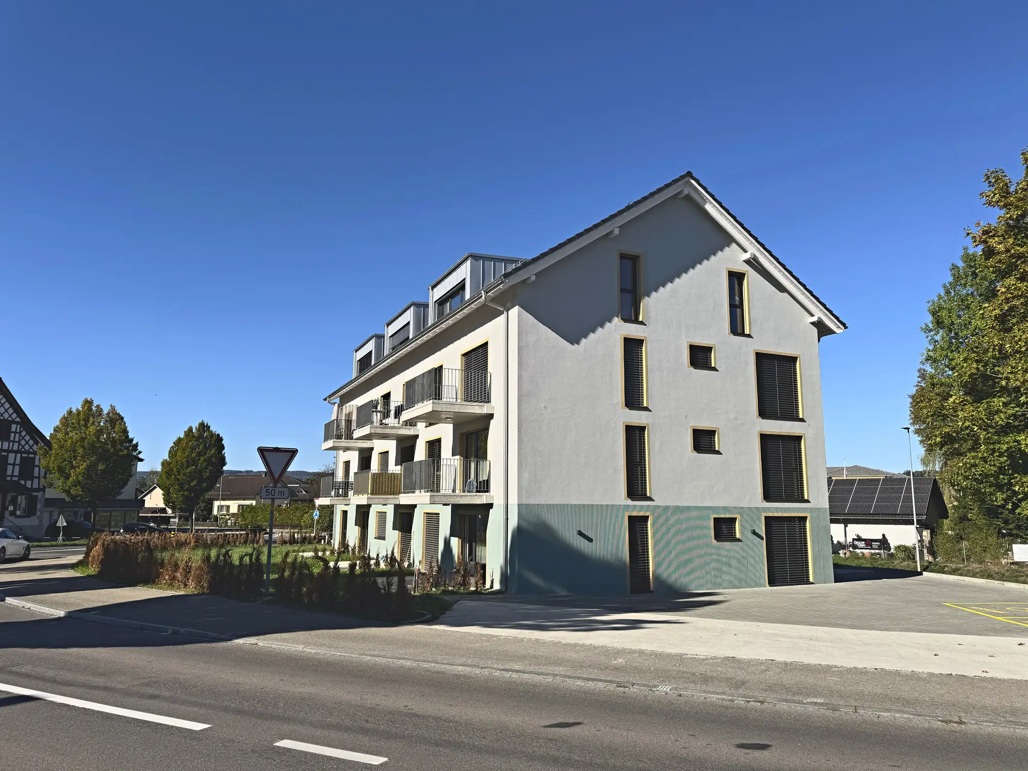 Blick von der Kreuzung auf Haus und Vorplatz, Dorfbebauung im Hintergrund