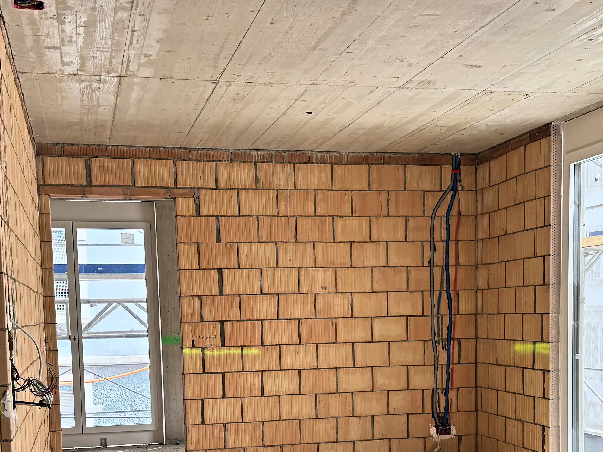 Zimmer mit Backsteinwand, Sichtbetondecke und Fenstertür zum Gerüst