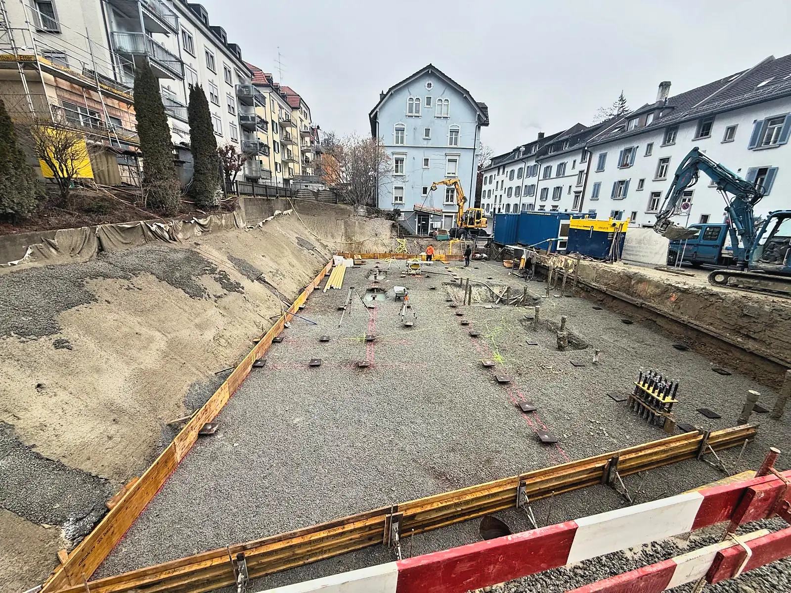 Ausgehobene Baugrube mit Randschalung und Pfahlköpfen im Quartier