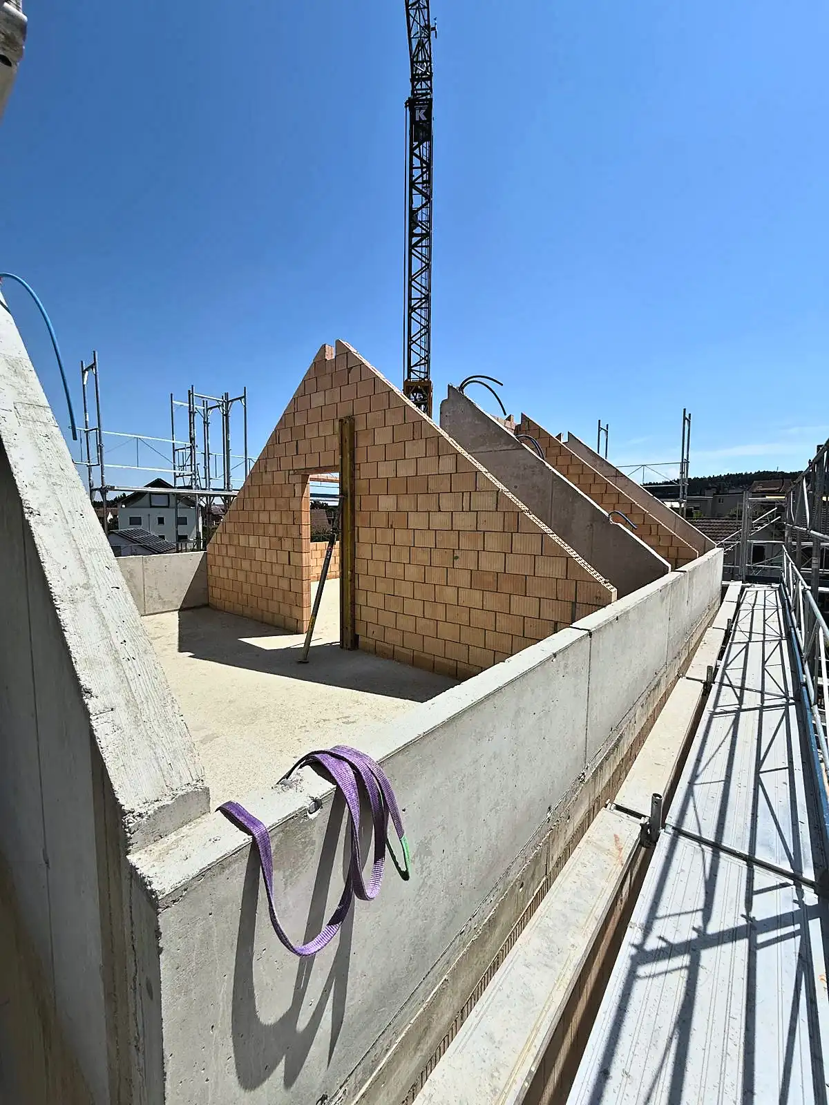 Dachaufbau im Rohbau, Giebelmauerwerk und Kran über der Betonbrüstung
