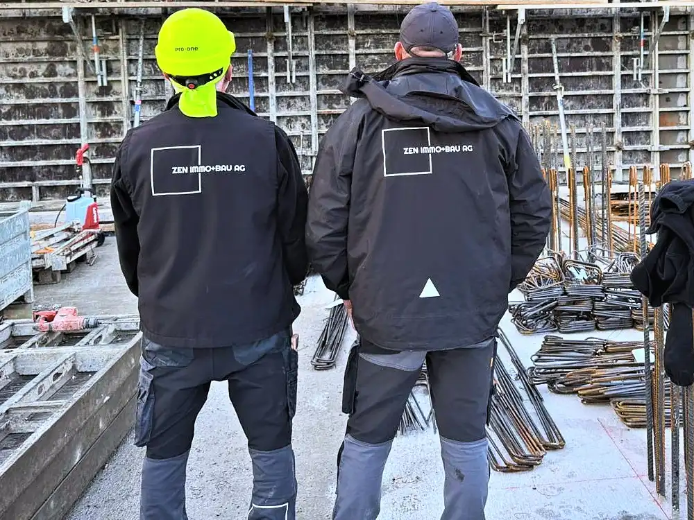 Zwei Mitarbeitende mit Zen-Jacke vor der eingeschalten Untergeschosswand